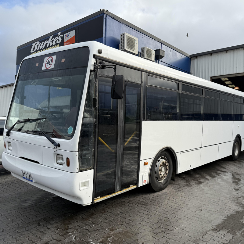 White route bus parked on wet brick paving outside a workshop