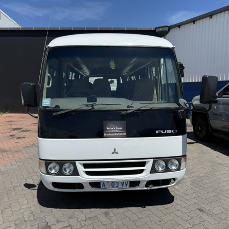 Front of a white minibus parked on brick paving outside a shed