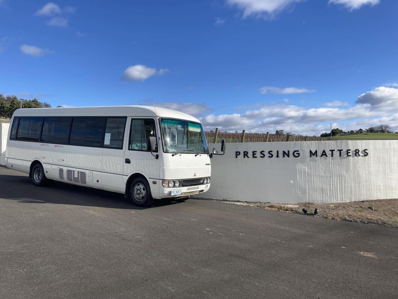 White minibus parked beside a wall signed Pressing Matters