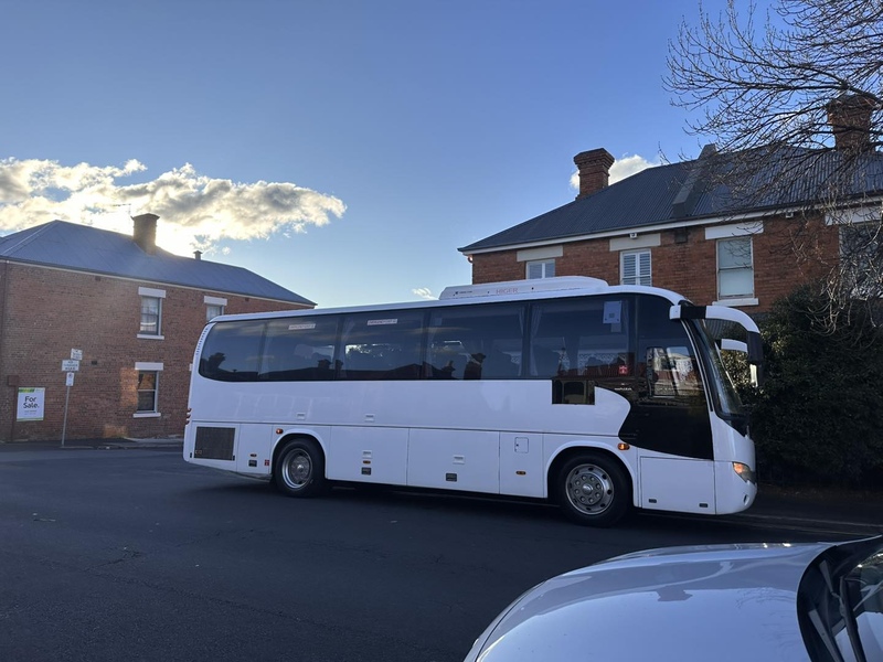 White coach parked on a street in front of old red-brick buildings