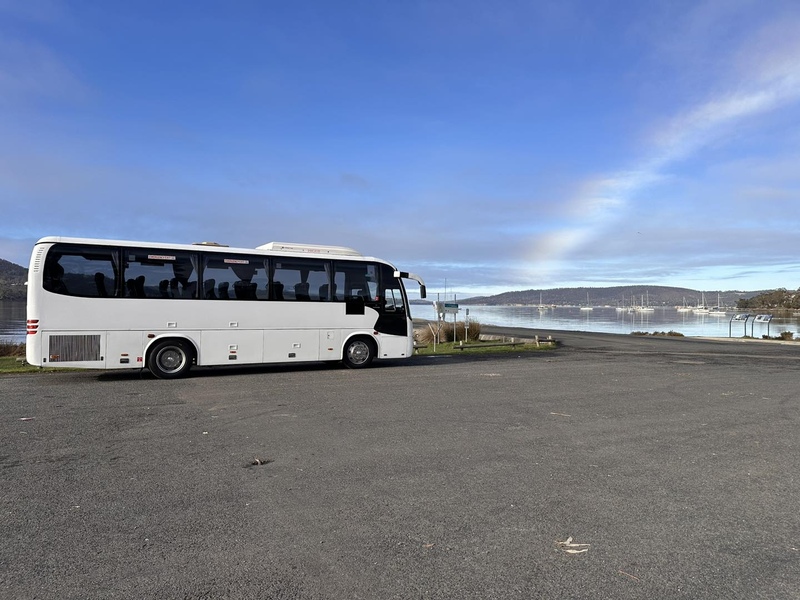 White coach parked in a waterfront car park with yachts on the bay behind
