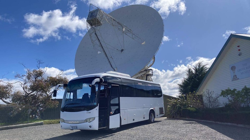 White coach parked in front of a large satellite dish under a blue sky