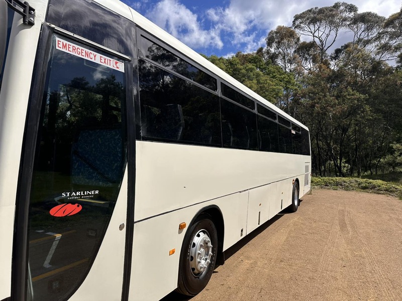 Low-angle view of a white coach's emergency exit door and side, parked on a dirt clearing