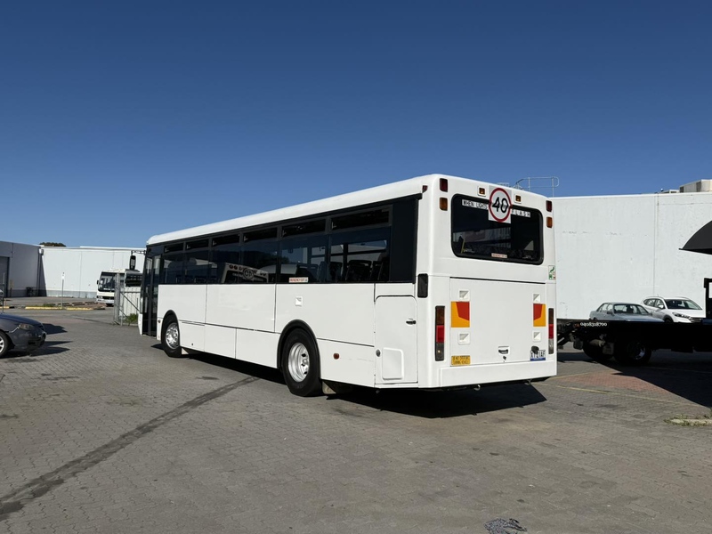 Rear of a white route bus parked in a sunny industrial car park