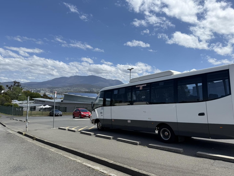 White midi bus with grey lower panels in a car park, mountains behind