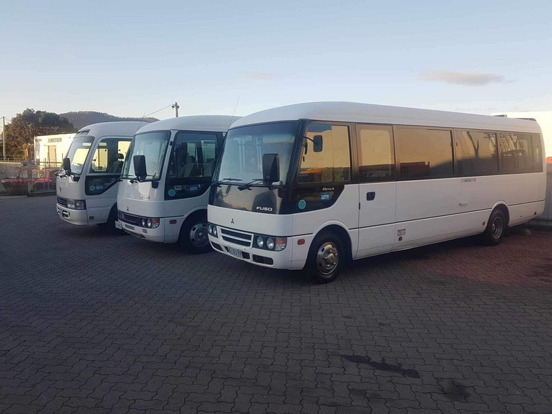Three white minibuses parked side by side on brick paving