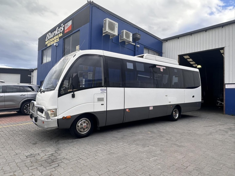 White midi bus with grey lower panels parked outside a blue workshop