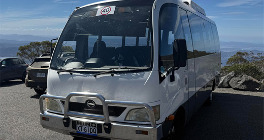 Hino R8 bus parked at a mountain lookout with views behind