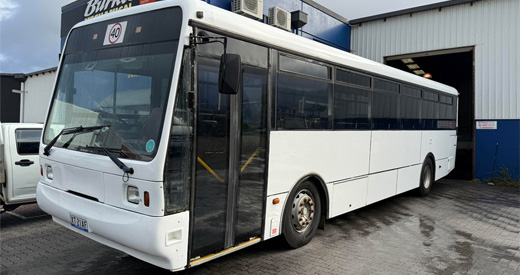Scania Orana bus parked on wet paving outside a workshop