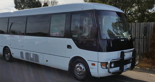 Mitsubishi Rosa Deluxe minibus with a bull bar parked beside a fence