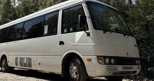 Mitsubishi Rosa minibus parked on gravel in front of gum trees